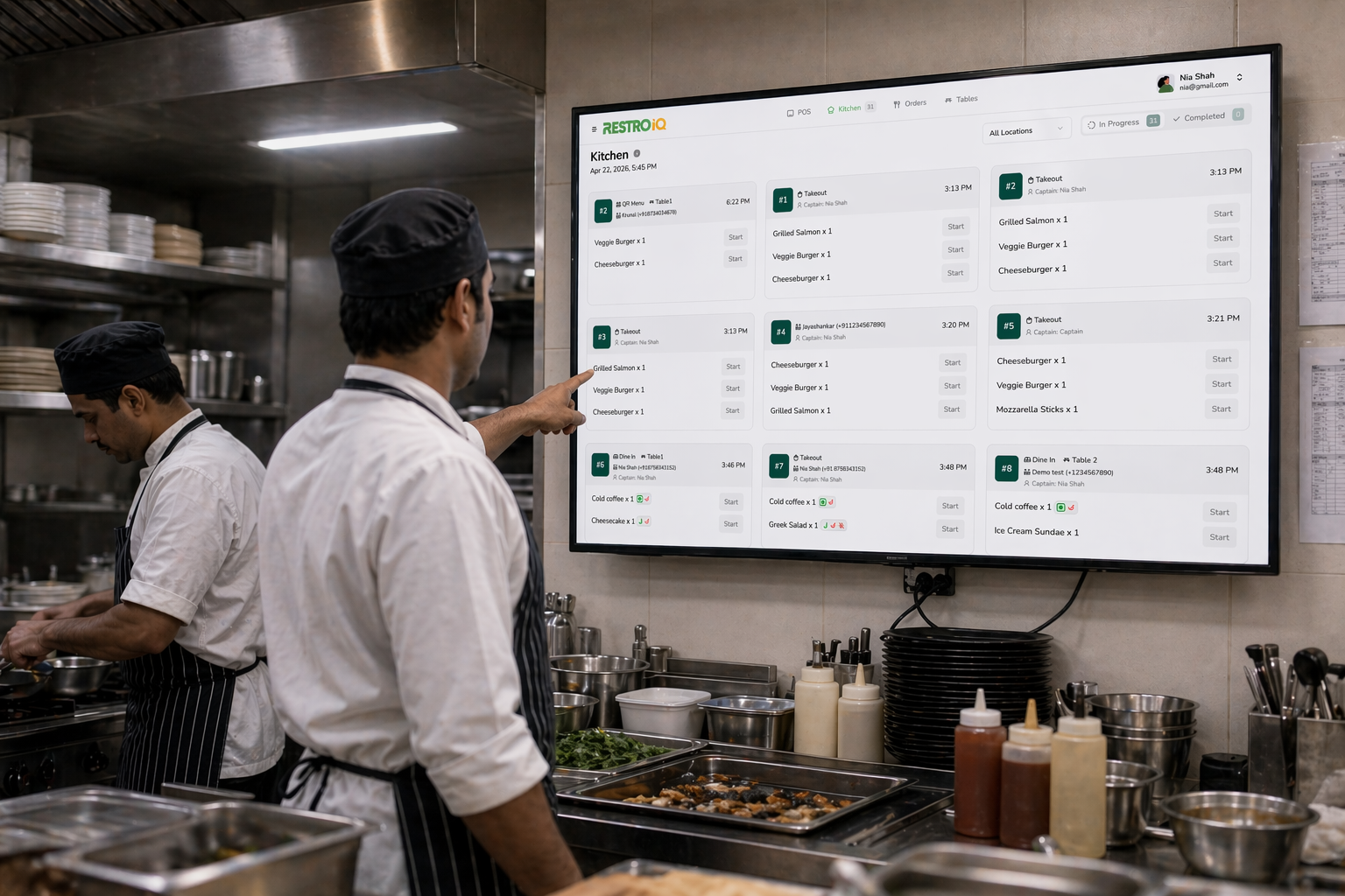 Chefs in a restaurant kitchen reading live orders on the RestroIQ Kitchen Display System screen